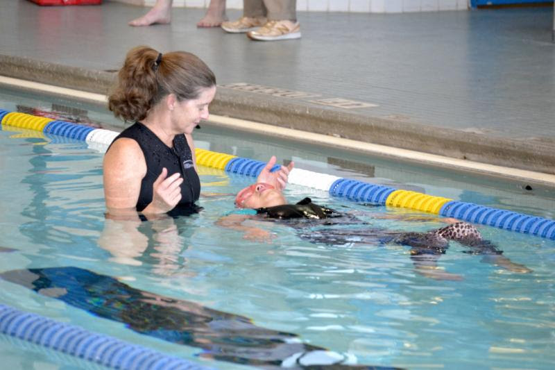 A swim instructor helps a young girl swim backstroke.