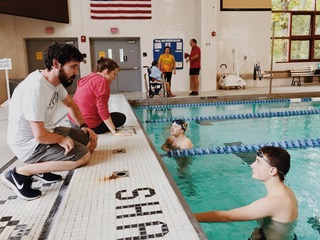 A coach provides guidance to adaptive athletes at swim team.