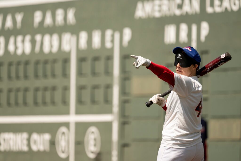 Karen Nagle in a Boston Strong beep baseball uniform, pointing outwards as she gets ready to bat at Fenway Park