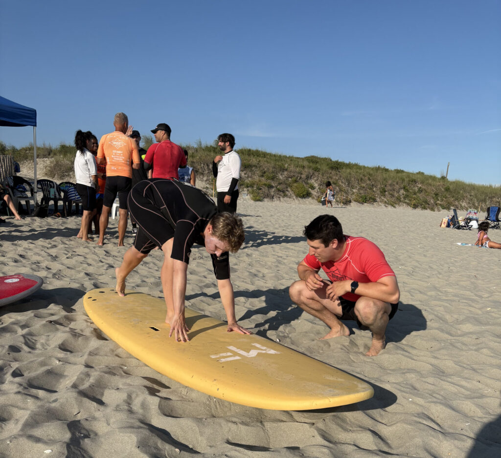 Karen Nagle being instructed by a man while she stands on a surfboard